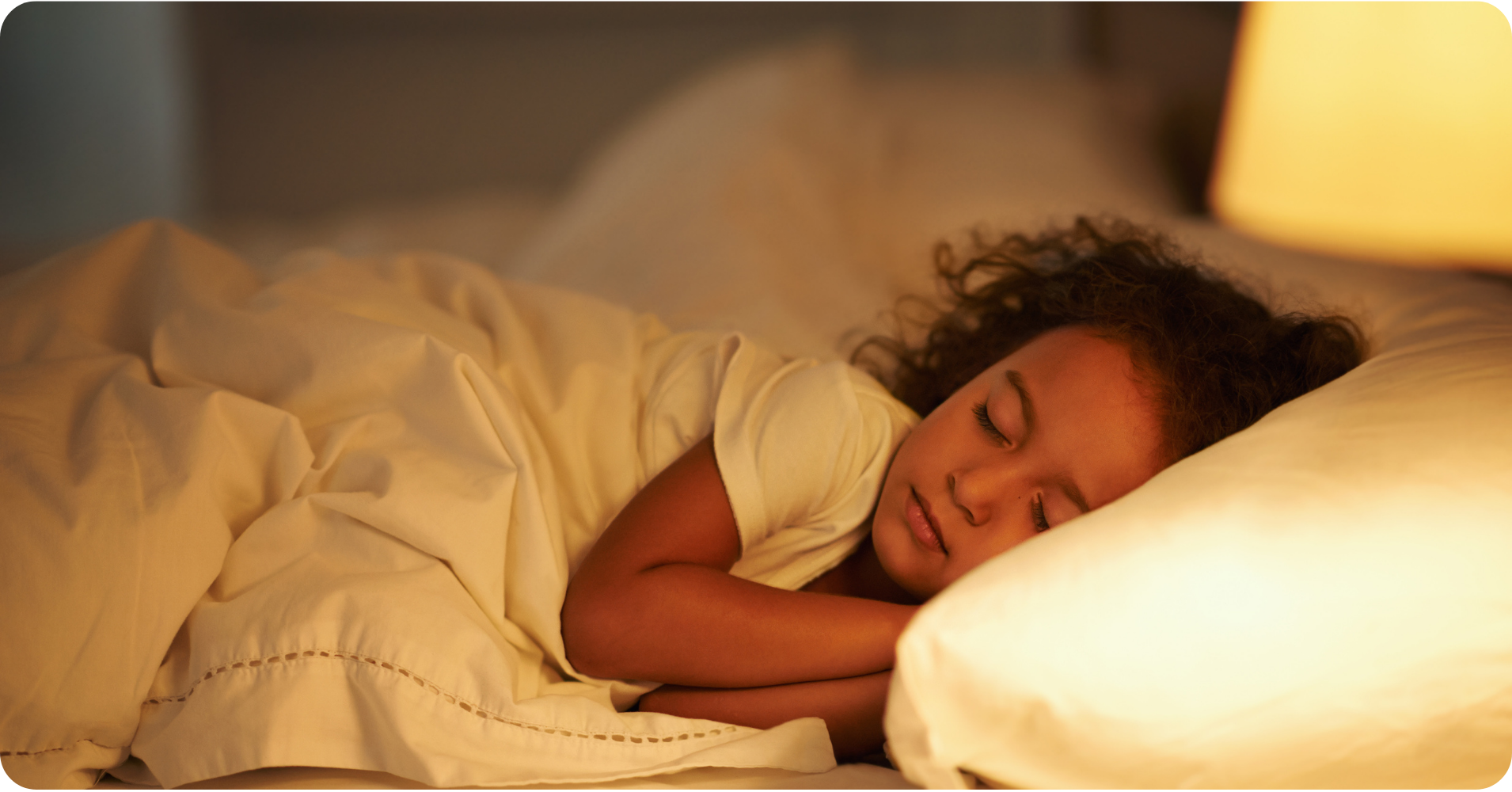 Slapend kind in bed met warm zacht licht in de slaapkamer, ontspannen en rustig onder een wit dekbed