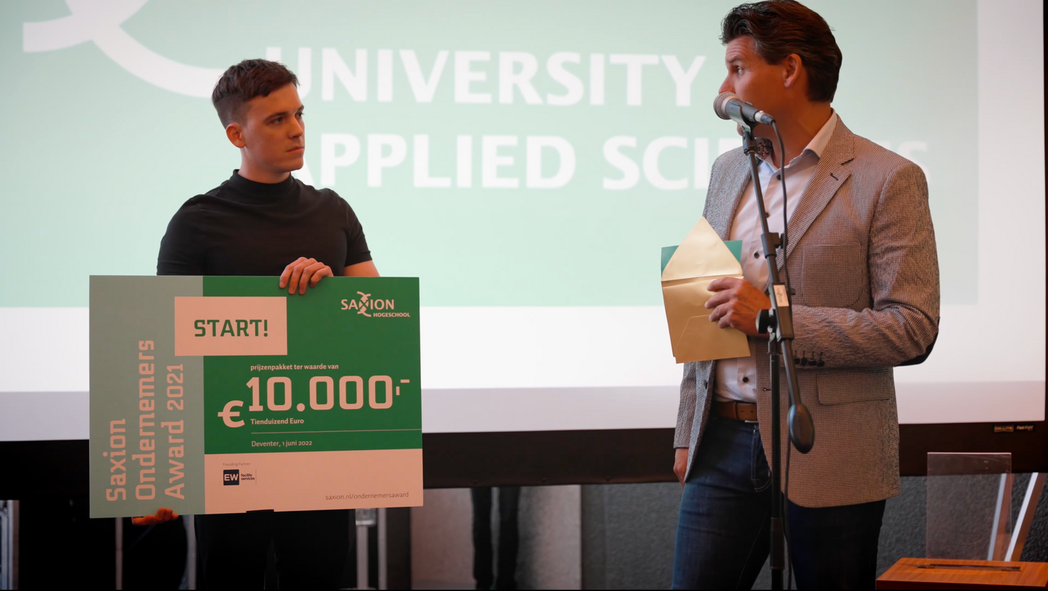 Eli staat met een cheque van 10.000 euro op het podium.