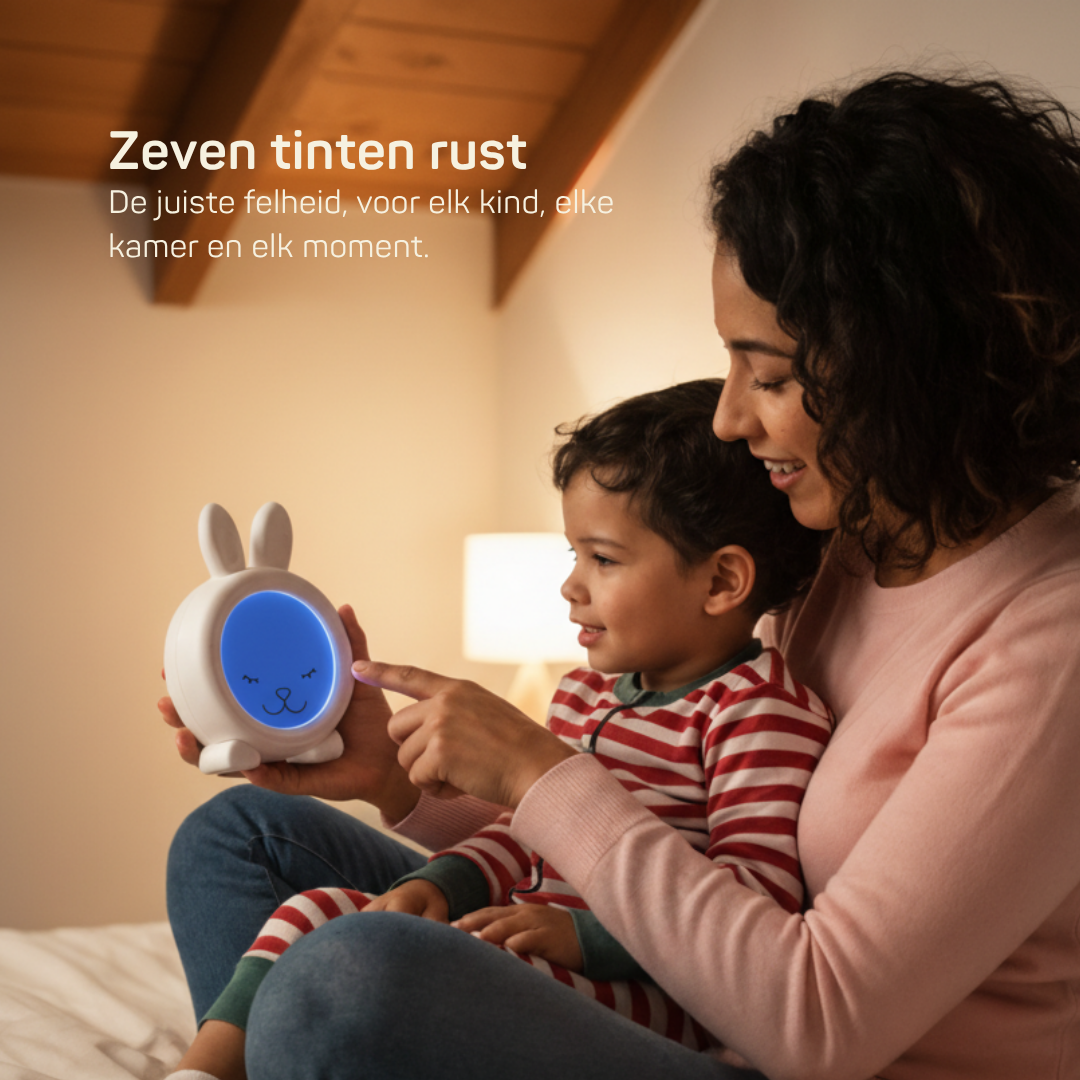 Moeder en kind zitten samen op bed met een witte slaaptrainer in de vorm van een konijn,  instelbaar in zeven helderheidsniveaus voor elke kamer en elk moment van de dag.