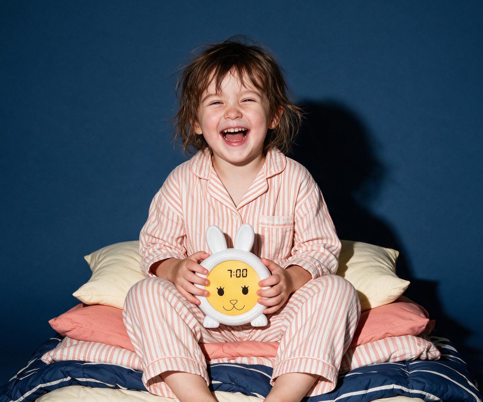 Lachend kind in gestreepte pyjama met slaaptrainer Konijn op schoot