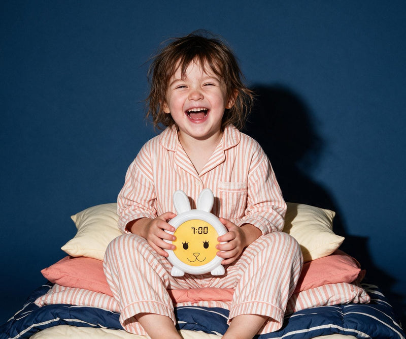 Lachend kind in gestreepte pyjama met slaaptrainer Konijn op schoot